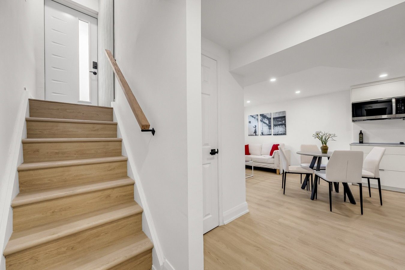 Een modern interieur met een houten trap, een eetgedeelte met witte meubels en een keuken met een magnetron.
