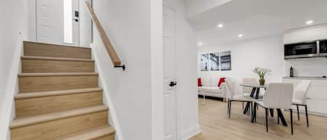 A modern interior with a wooden staircase, a dining area with white furniture, and a kitchen with a microwave.