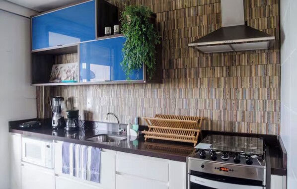 A modern kitchen with a stove, sink, and blue cabinets. - Mandara Kauai: Paraíso à Beira-Mar em Porto das Dunas! Apt com 4 Quartos! (Aquiraz)