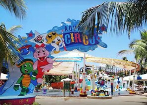 A theme park entrance with a colorful sign featuring cartoon characters and the words 'AQUA CIRCUS.' - Mandara Kauai: Paraíso à Beira-Mar em Porto das Dunas! Apt com 4 Quartos! (Aquiraz)