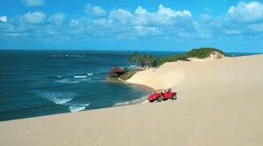 Paisagem costeira com duna, oceano e um veículo vermelho.