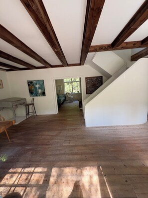 Interior com vigas de madeira, uma escada e vista para um quarto com janela.