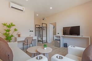 A modern, well-lit hotel room with a flat-screen TV, a desk with a chair, a small table with a plant, a sofa, and a coat rack.