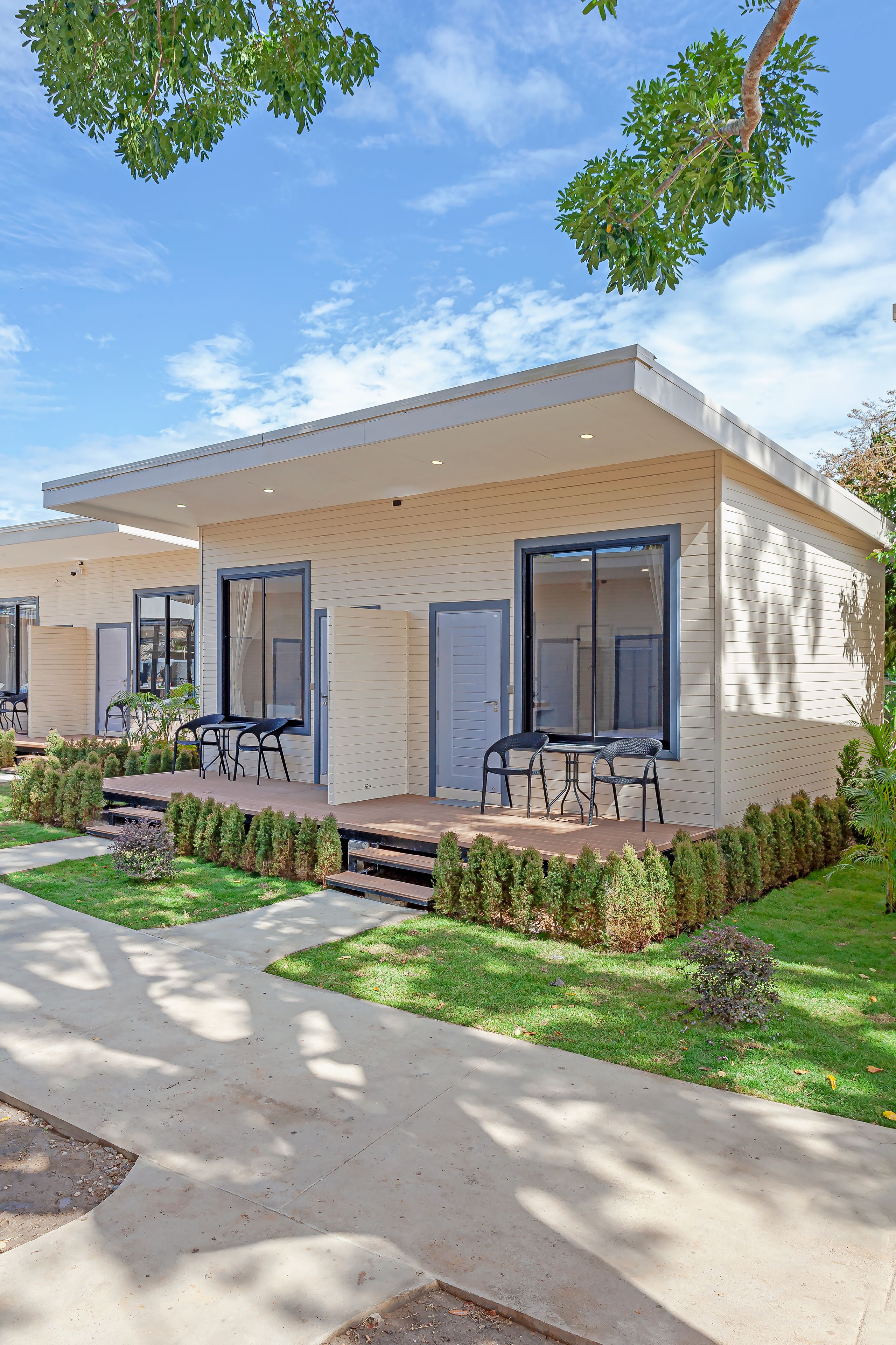 A modern two-story house with a covered patio, a dining area with chairs, and a well-maintained lawn.
