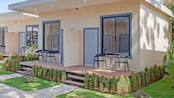 A modern two-story house with a covered patio, a dining area with chairs, and a well-maintained lawn.