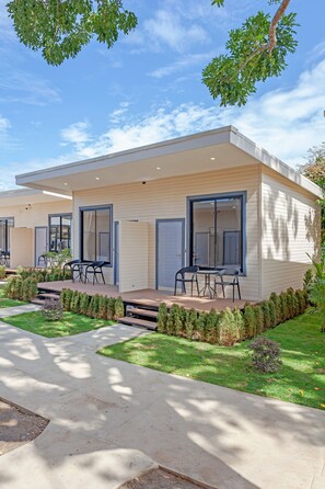 A modern two-story house with a covered patio, a dining area with chairs, and a well-maintained lawn.