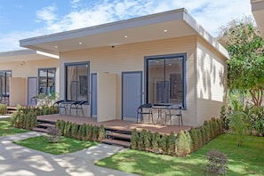 A modern residential building with a flat roof, large windows, and a covered patio area with outdoor seating.