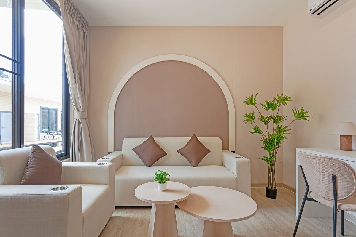 A modern living room with a sofa, two pillows, a small table, a potted plant, and a chair.