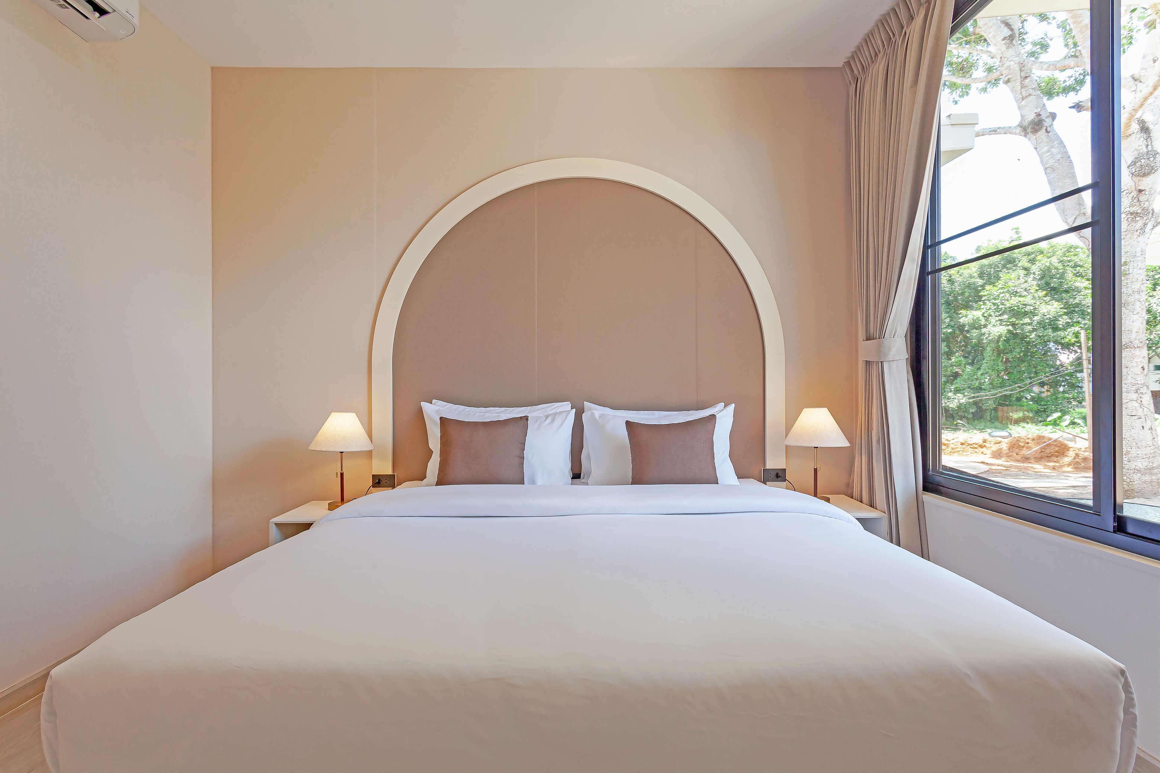 Quarto de hotel com uma cama grande, duas mesas de cabeceira e uma janela com cortinas.