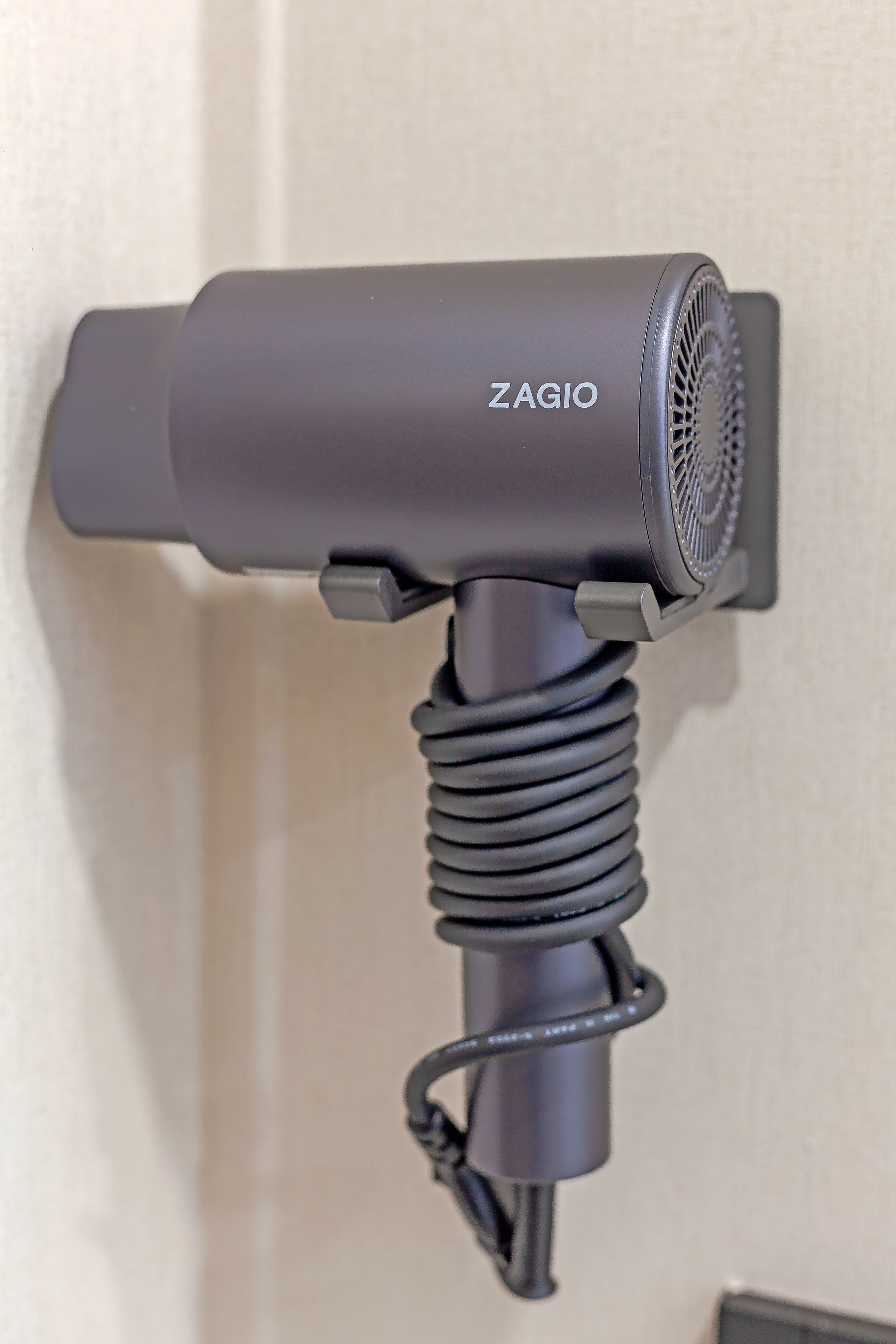 A wall-mounted hair dryer with a coiled cord.