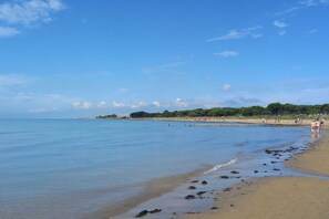 Ein Strand mit klarem Wasser, einem Sandufer und einem Steg, der ins Wasser ragt.