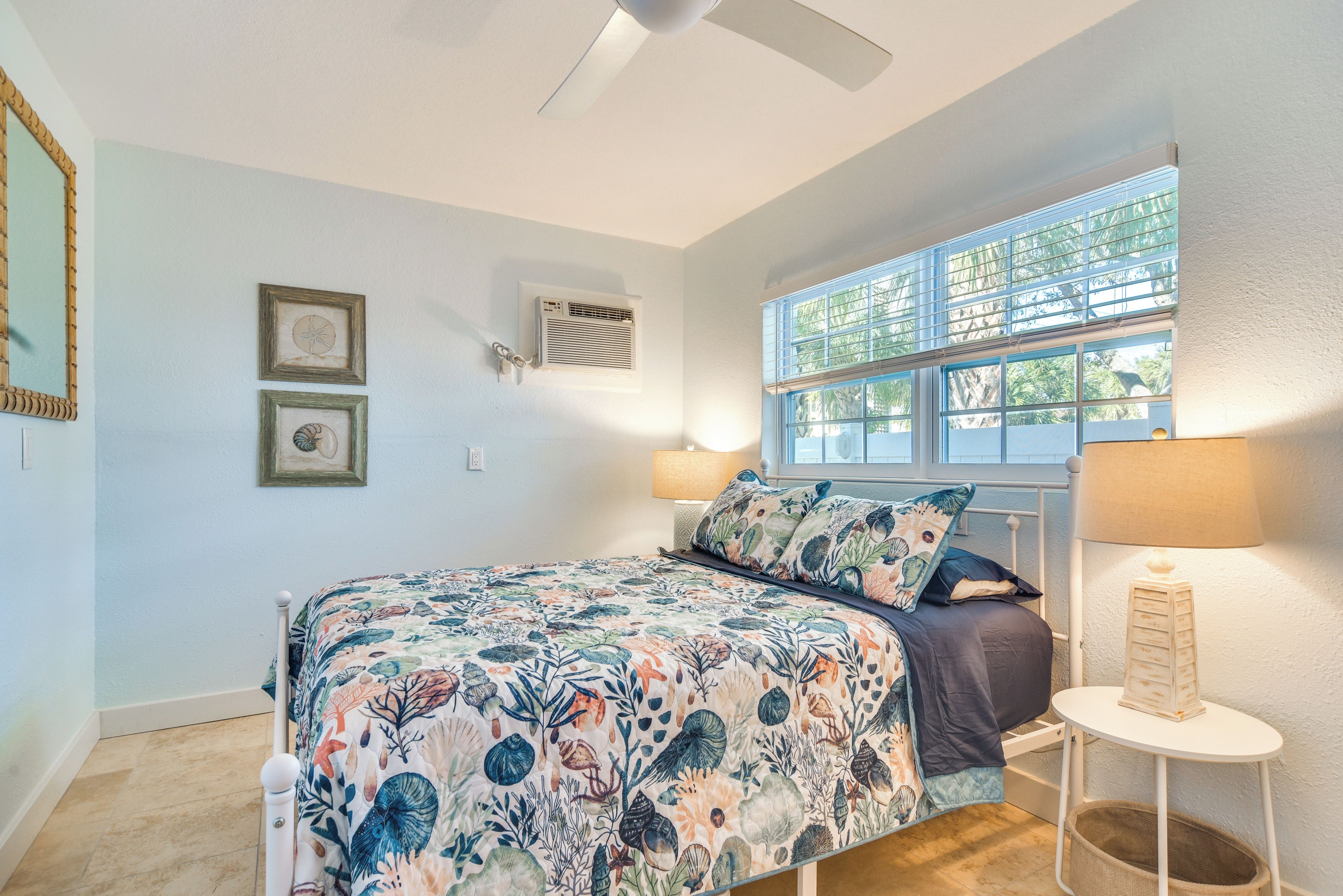 A bedroom with a bed, a window with a view, a ceiling fan, and wall-mounted air conditioning.