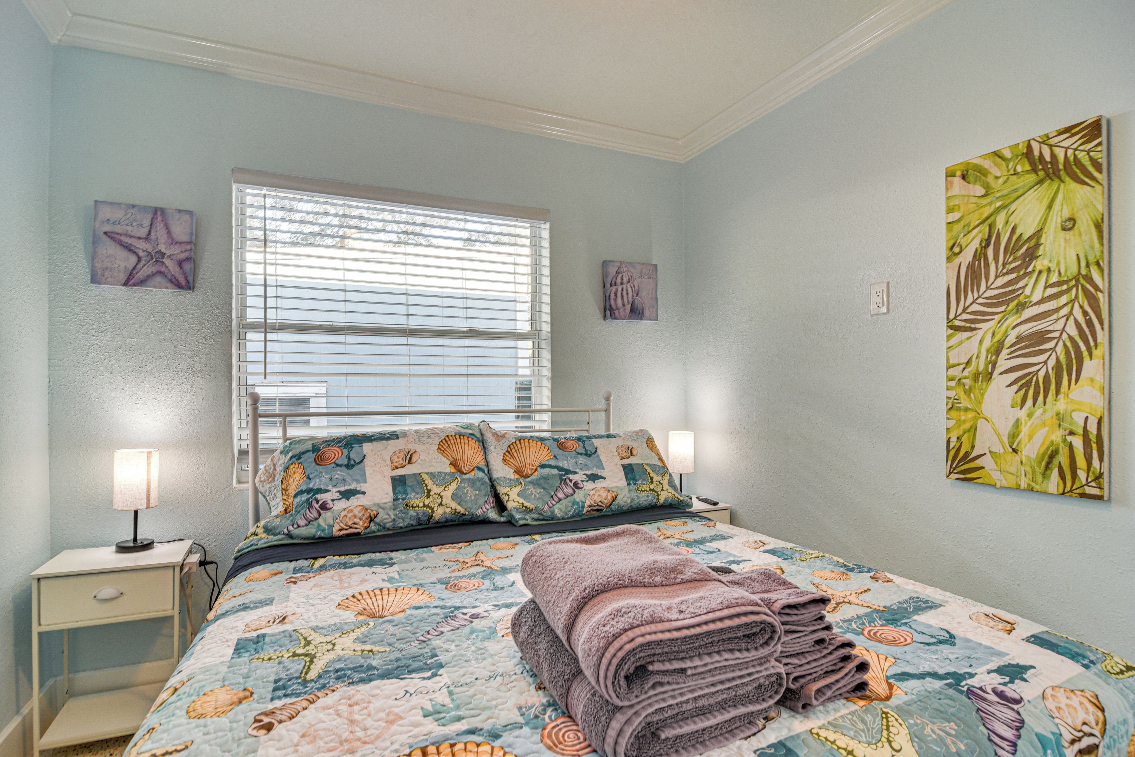 A bedroom with a bed, nightstands, and artwork on the walls.