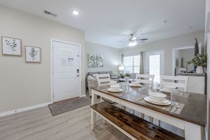A dining area with a wooden table set for four, a ceiling fan, and a door with a bulletin board. - Condo Near Branson Strip: Close to It All! (Branson)