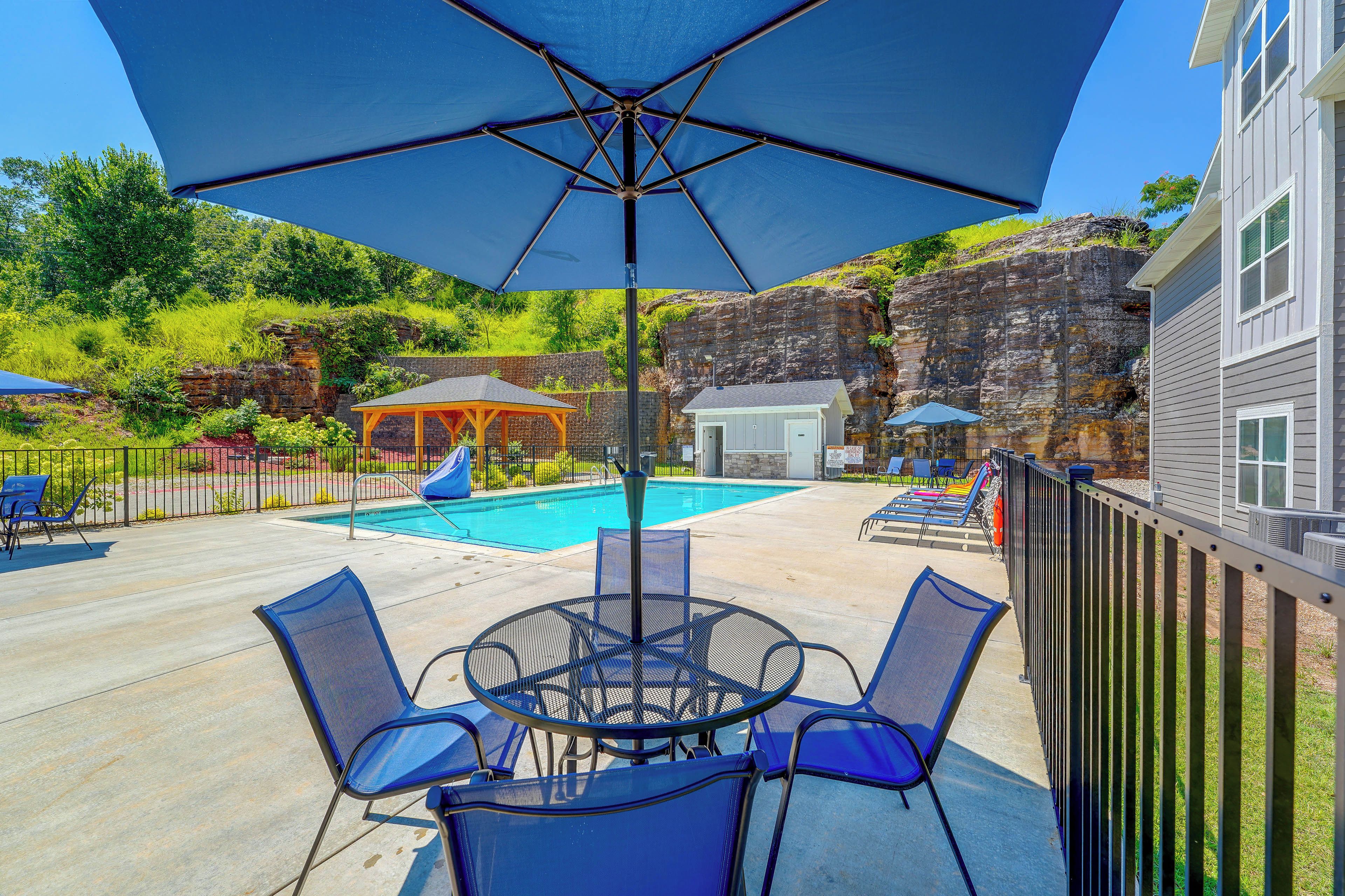 A pool area with a covered seating area, lounge chairs, and a small building.