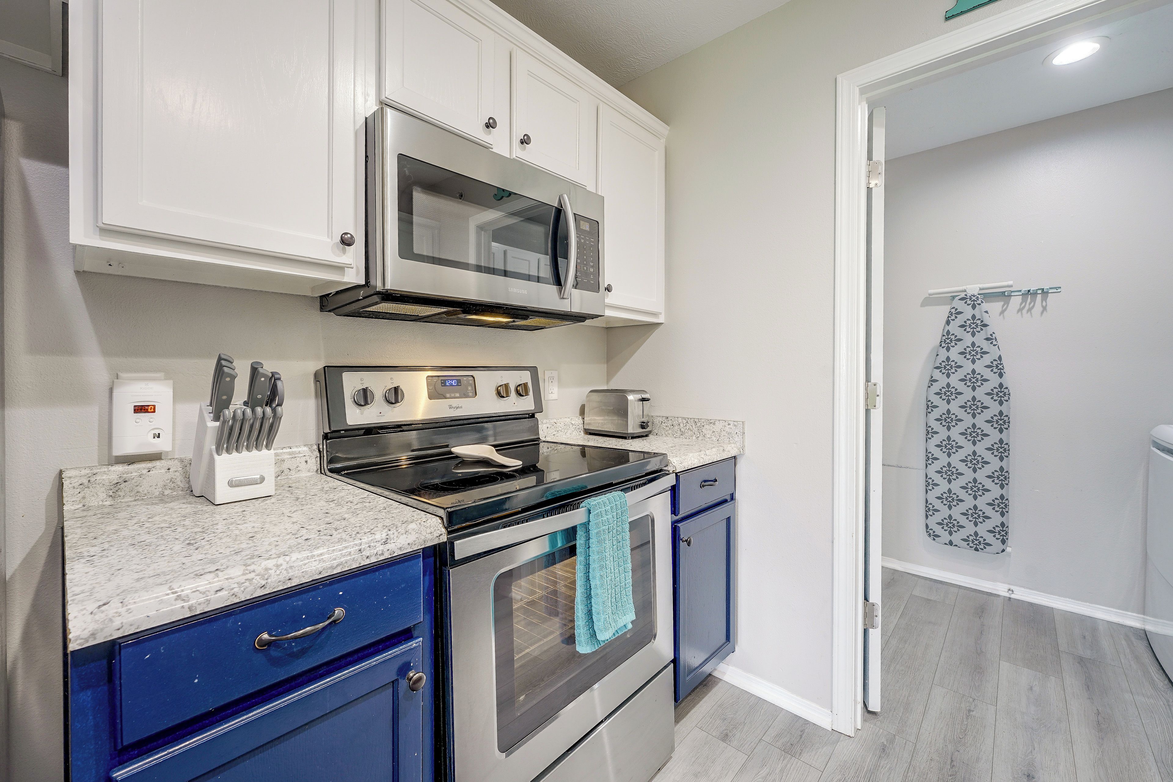 A compact kitchen with white cabinets, a microwave, a stove, and a toaster.