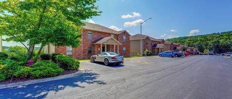 A parking lot with multiple cars, a brick building with a garage, and a tree-lined street.