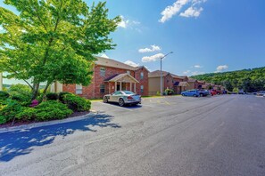 A parking lot with multiple cars, a brick building with a garage, and a tree-lined street. - Perfect Location! Amazing Views & Close to It All! (Branson)