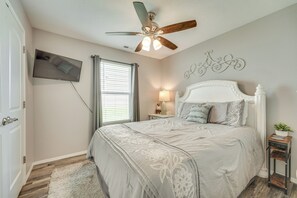 A bedroom with a bed, a ceiling fan, a TV, a window with blinds, a bedside table with a lamp, and a decorative wall piece. - Branson Condo Near Shows, Dining & Table Rock Lake (Branson)