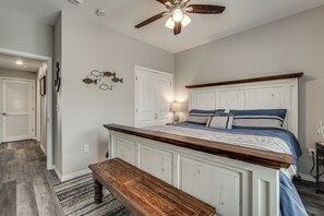 Une chambre à coucher avec un lit, un banc, un ventilateur de plafond et une porte.