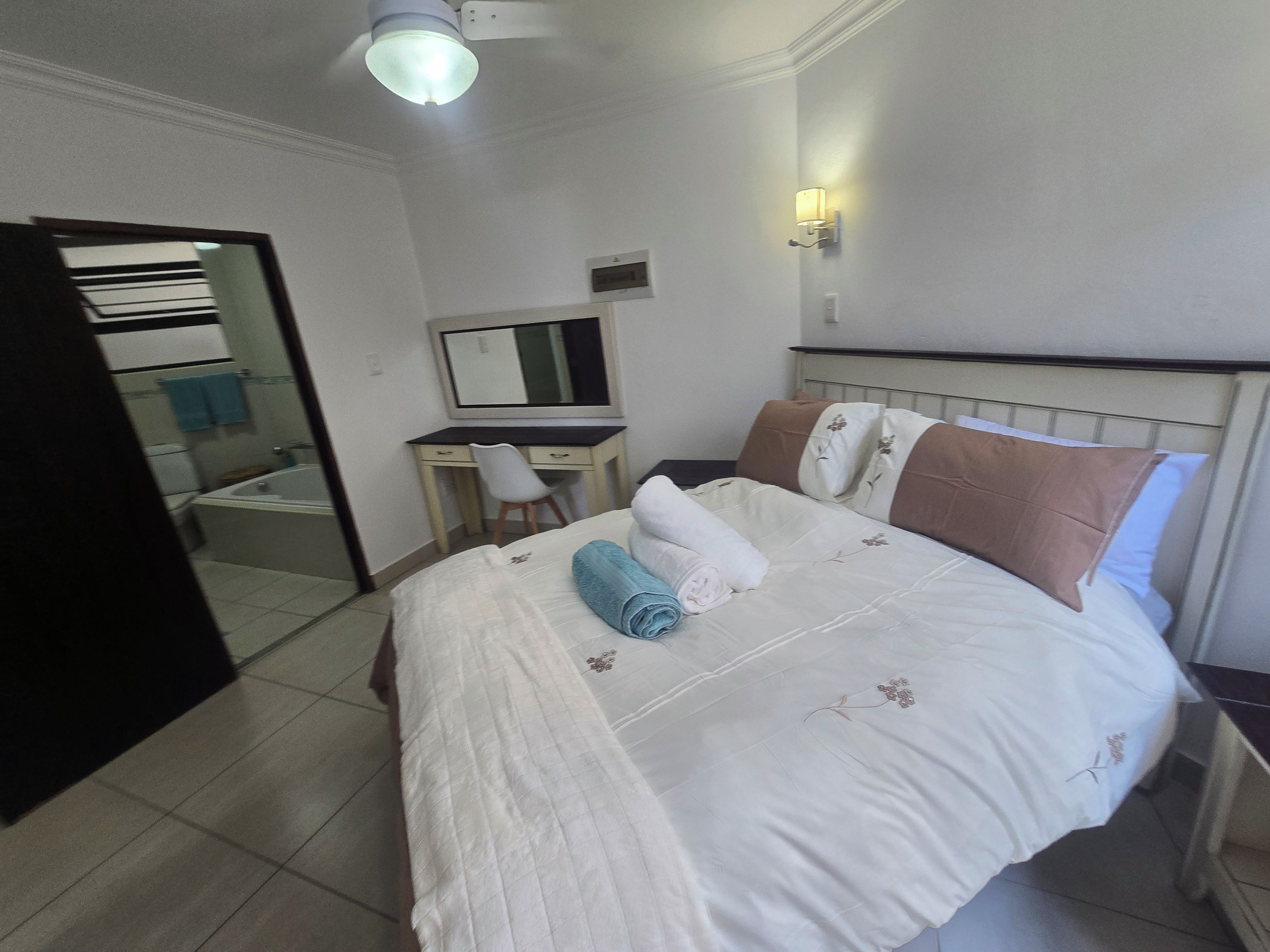 A hotel room with a bed, a desk, a chair, a mirror, and a bathroom visible through an open door.