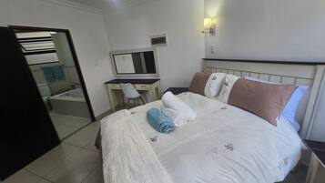 A hotel room with a bed, a desk, a chair, a mirror, and a bathroom visible through an open door.