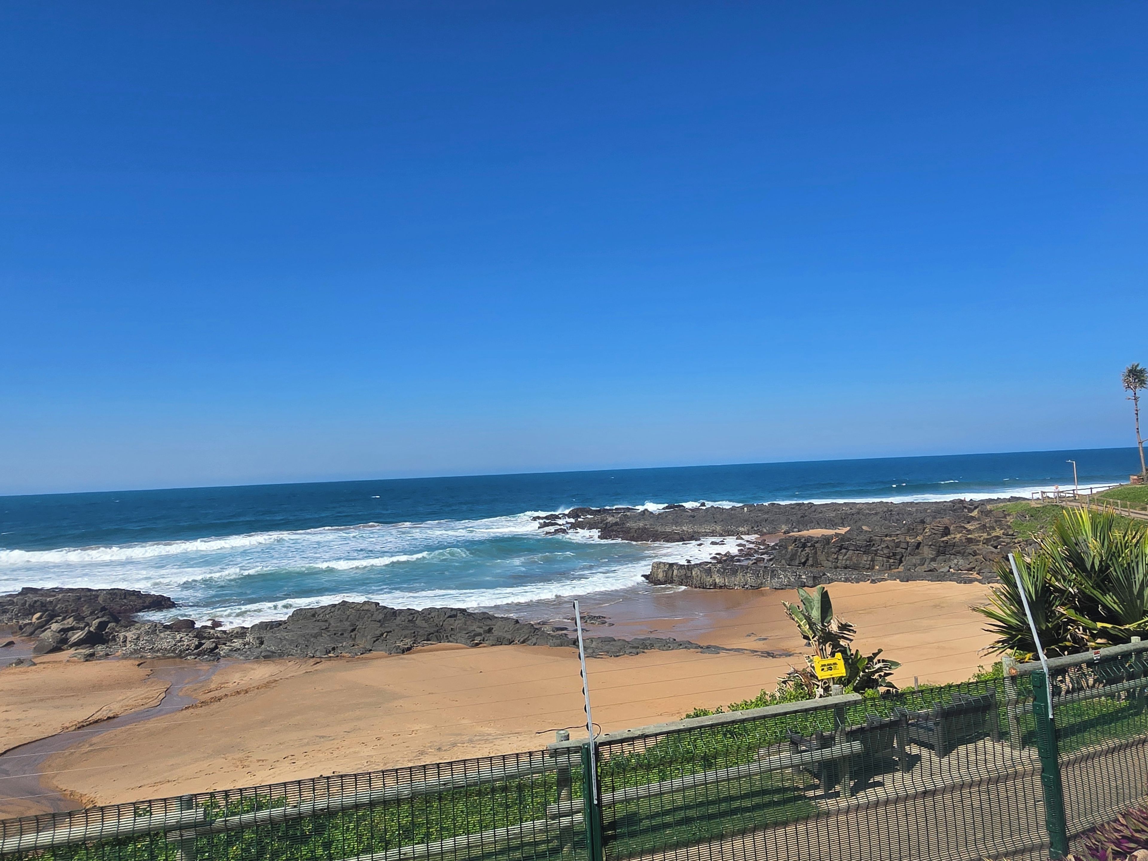Vista costera con playa arenosa, costa rocosa y cielo azul despejado.