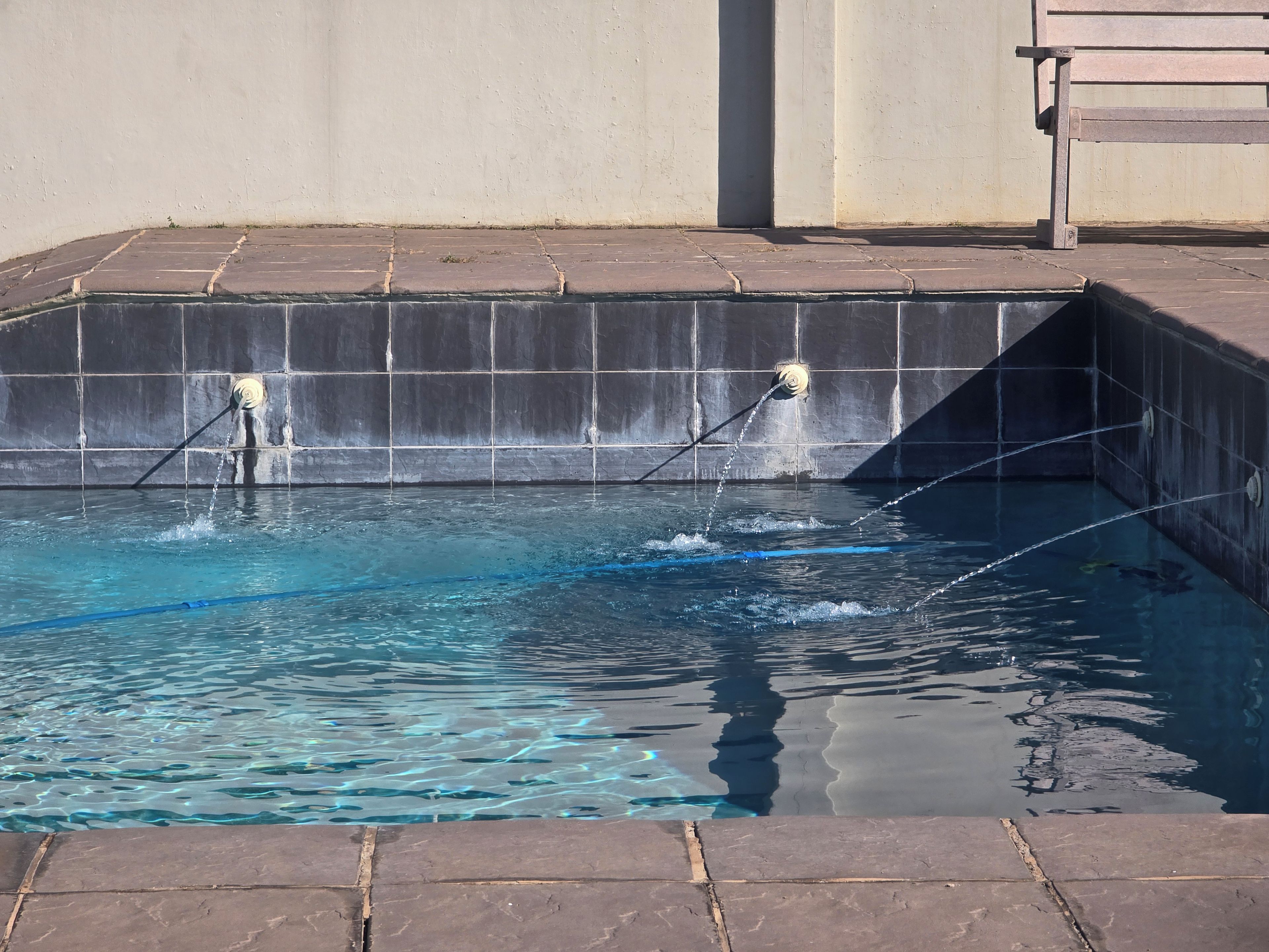 Piscina com água cristalina, borda azulejada e uma parede com cascata.