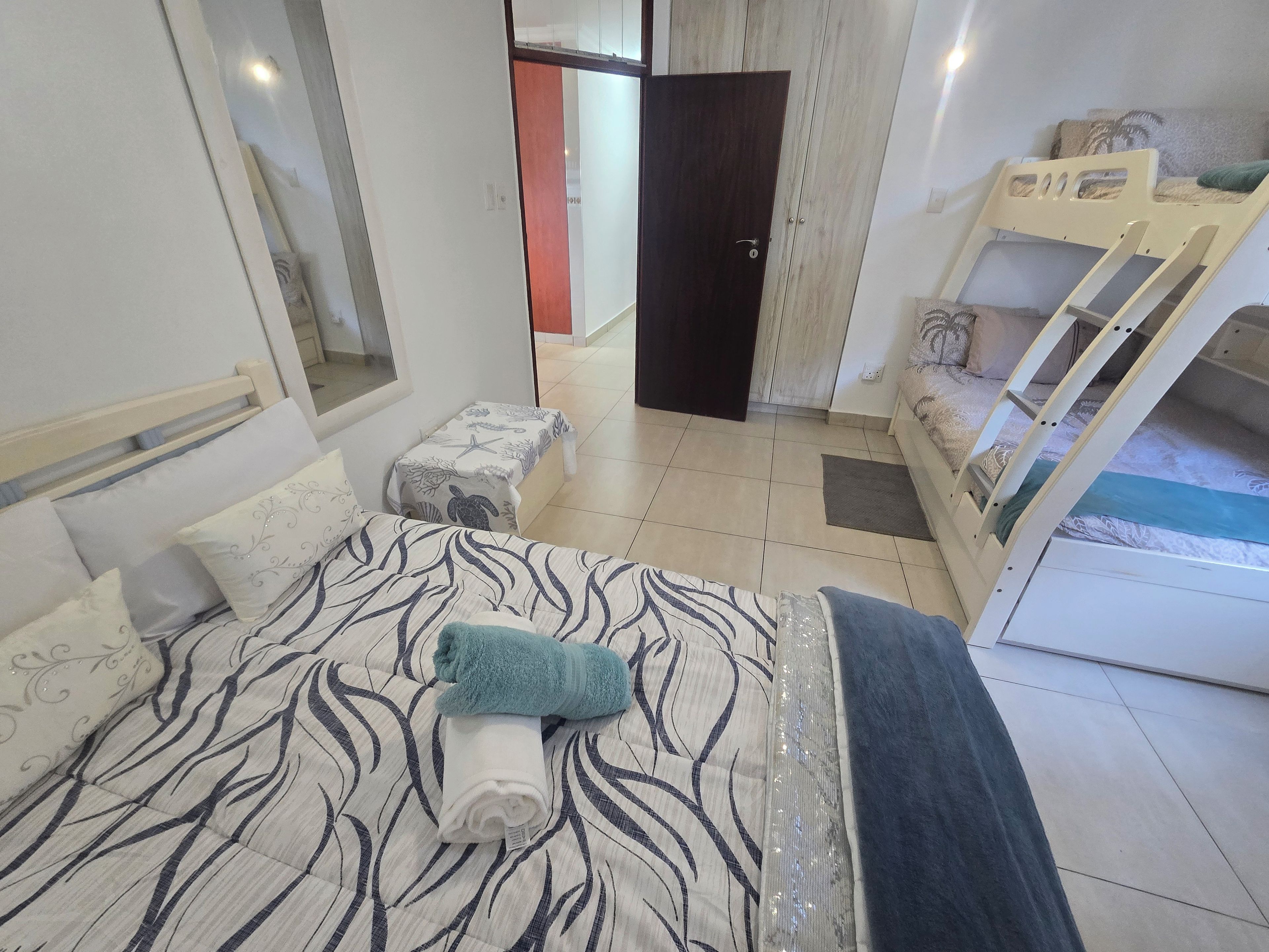A bedroom with a bed, a bench, a bunk bed, and a door leading to another room.