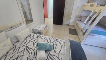 A bedroom with a bed, a bench, a bunk bed, and a door leading to another room.