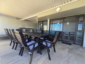 An outdoor patio with a dining table, chairs, and a sliding glass door leading to a covered area.