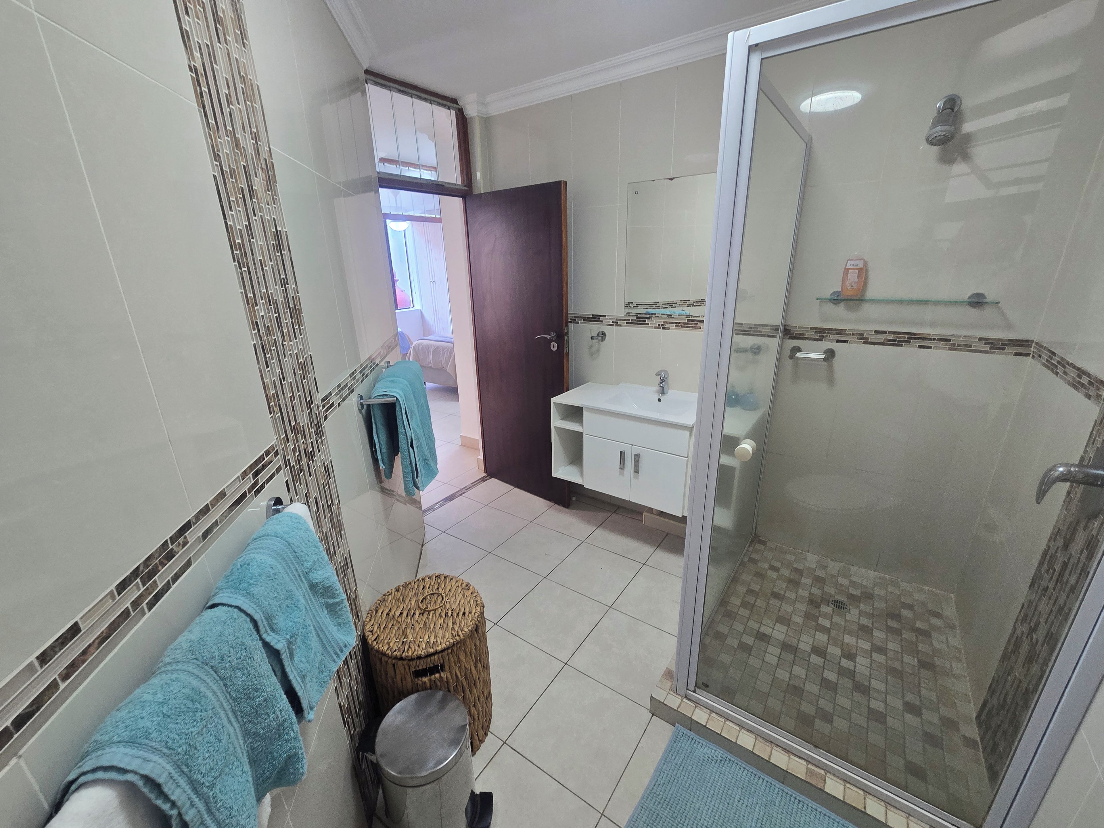 Un baño con cabina de ducha de vidrio, un lavamanos con espejo y un perchero para toallas.