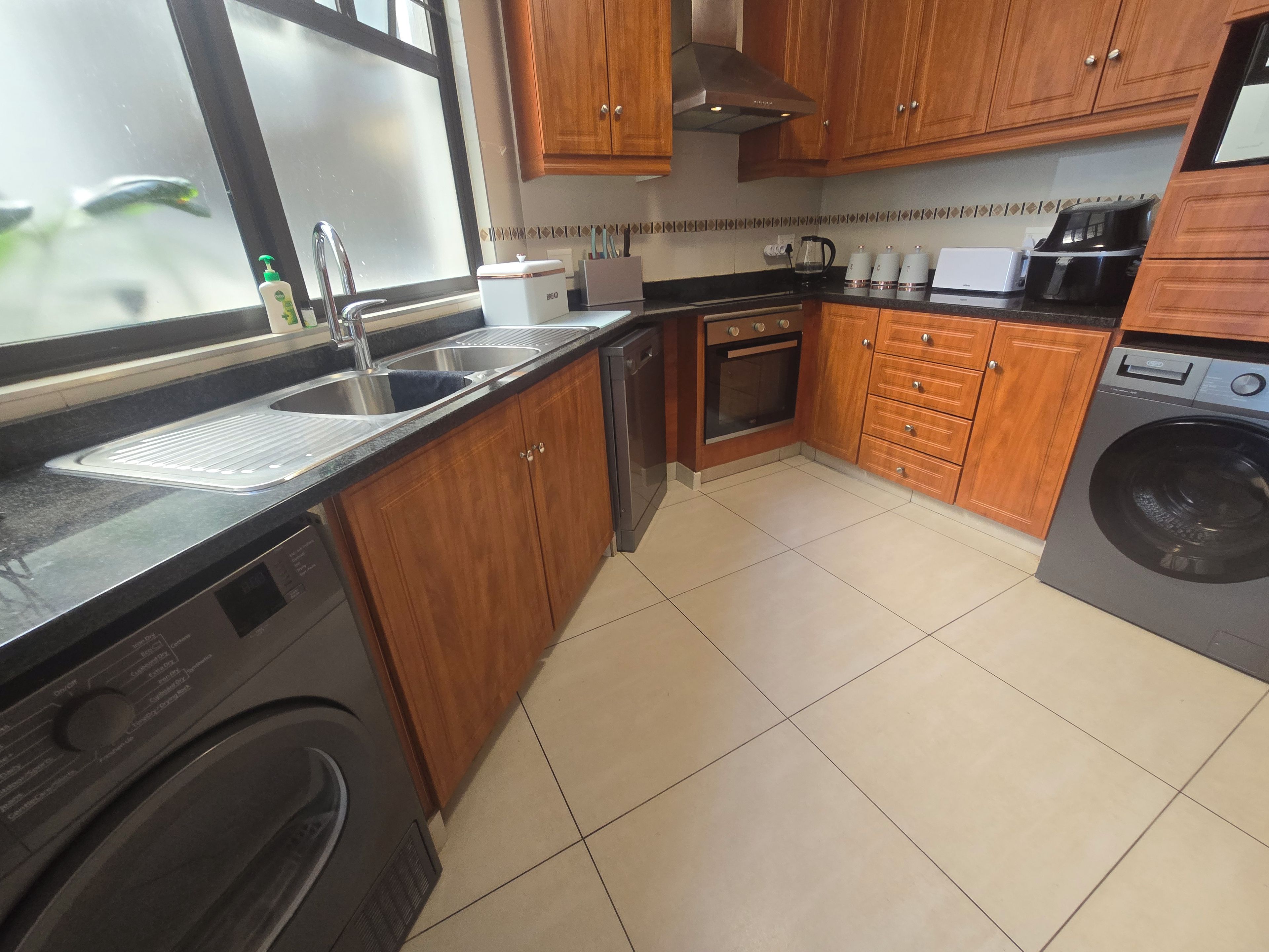 Een keuken met houten kastjes, een inbouwoven, een vaatwasser en een wasmachine.