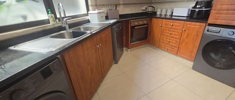 Une cuisine avec des meubles de rangement en bois, un four encastré, un lave-vaisselle et un lave-linge.