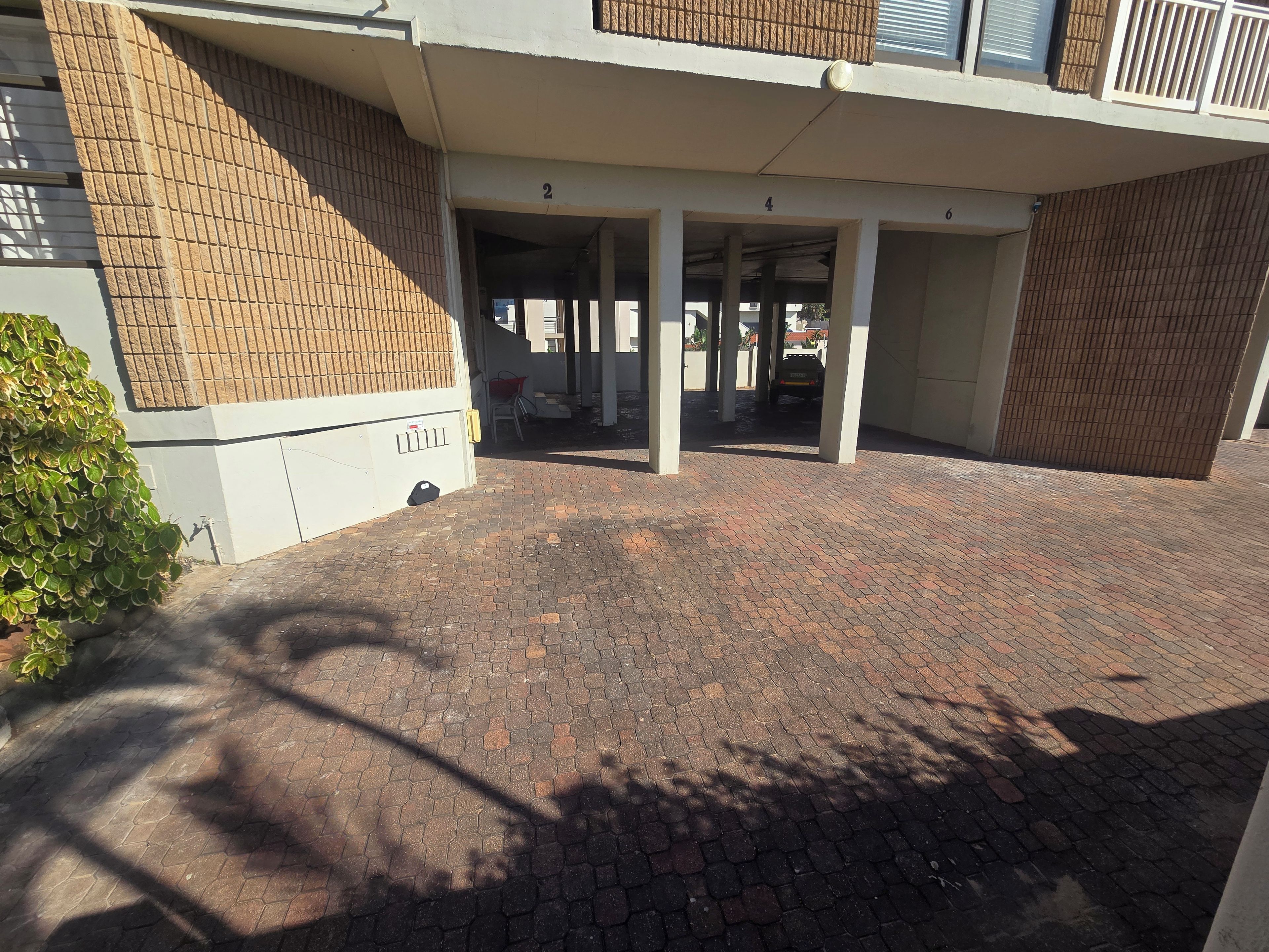 A covered parking area with a brick floor, a white building with numbered columns, and a visible door.