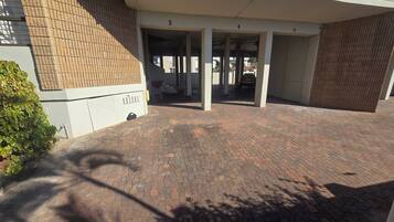 A covered parking area with a brick floor, a white building with numbered columns, and a visible door.