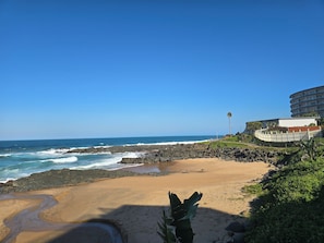 A beach with a rocky shoreline, a sandy area, and a building with multiple balconies.