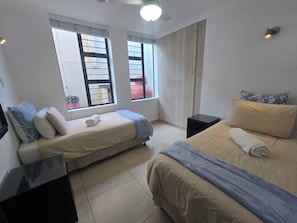 A bedroom with two beds, a nightstand, a window with a view, and a ceiling light.
