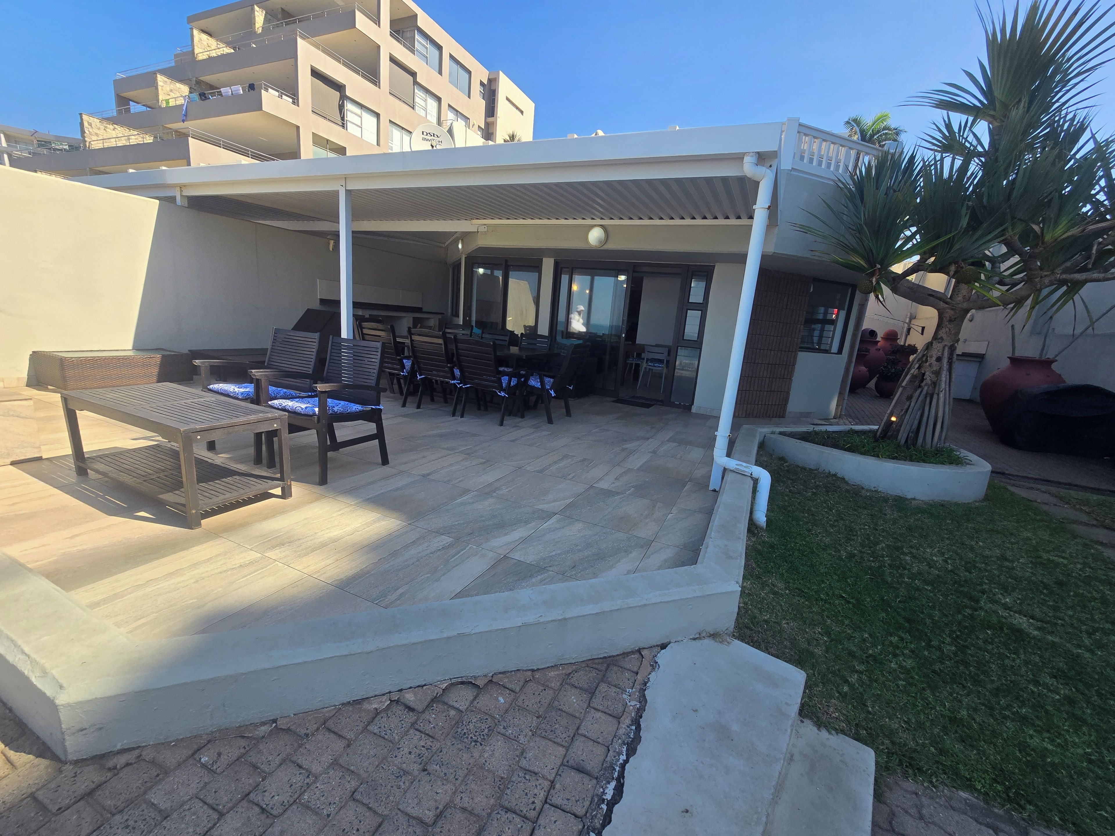 Un espace extérieur abrité, avec des tables et des chaises, un bâtiment en arrière-plan et un palmier.