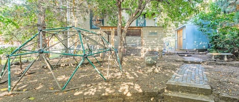 A garden with a metal play structure, a wooden bench, and a house with a fenced yard.