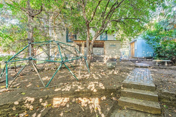 A garden with a metal play structure, a wooden bench, and a house with a fenced yard.