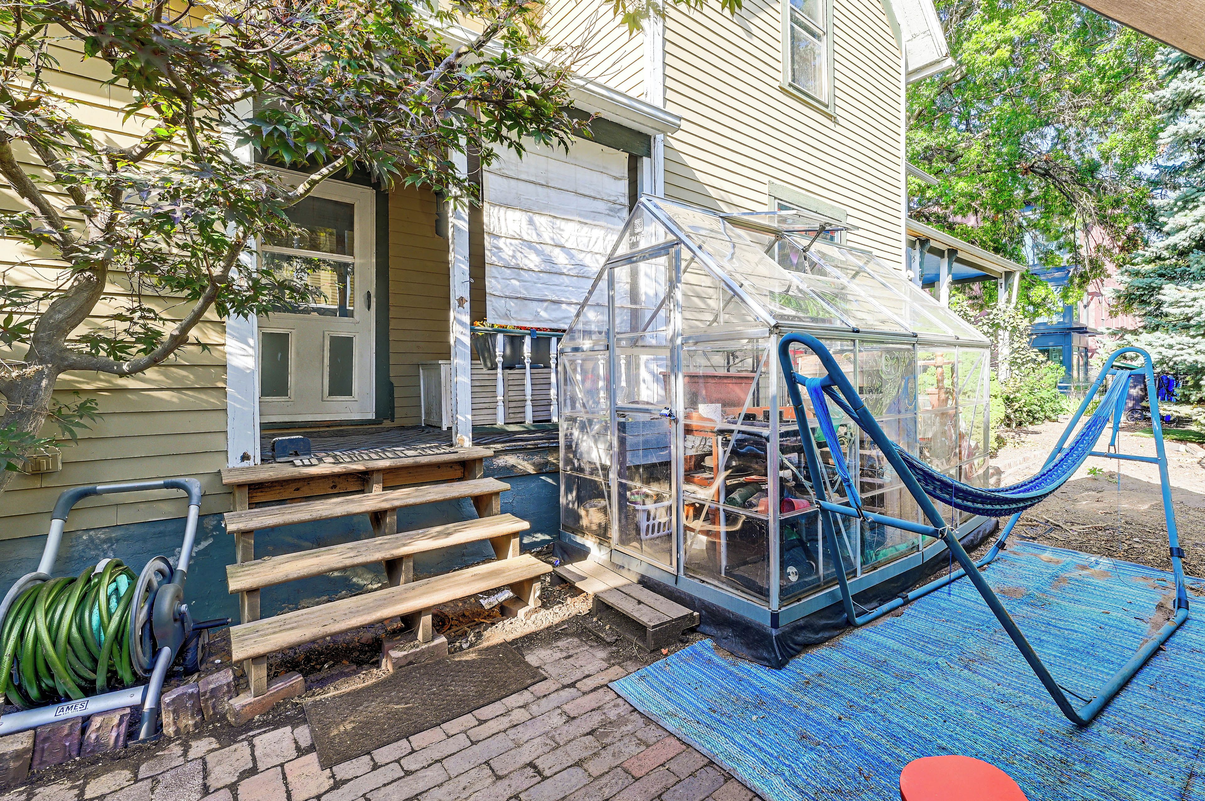 A house with a greenhouse, wooden steps, and a blue hammock.