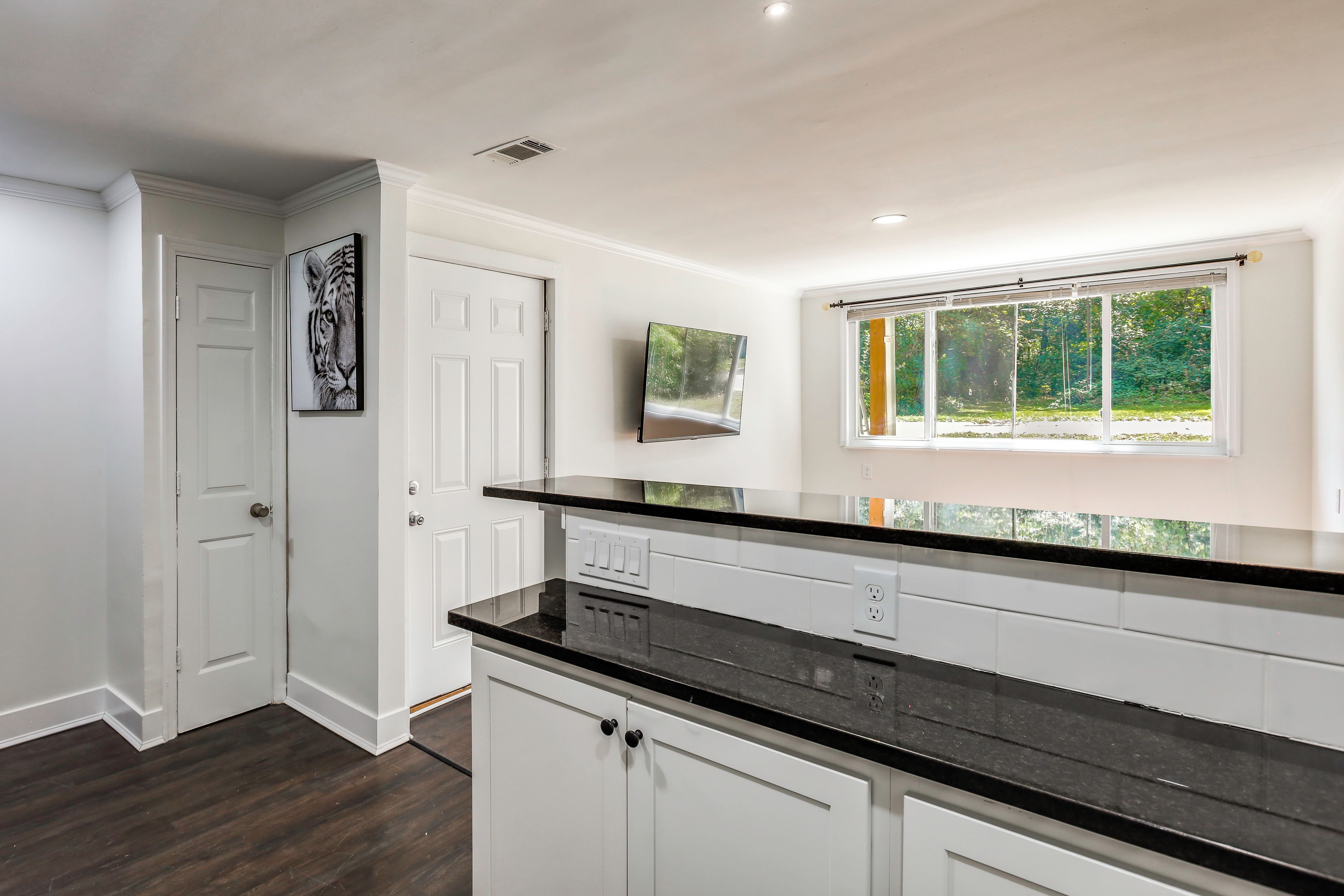 A kitchen with white cabinets, a black countertop, and a window with a view of greenery.