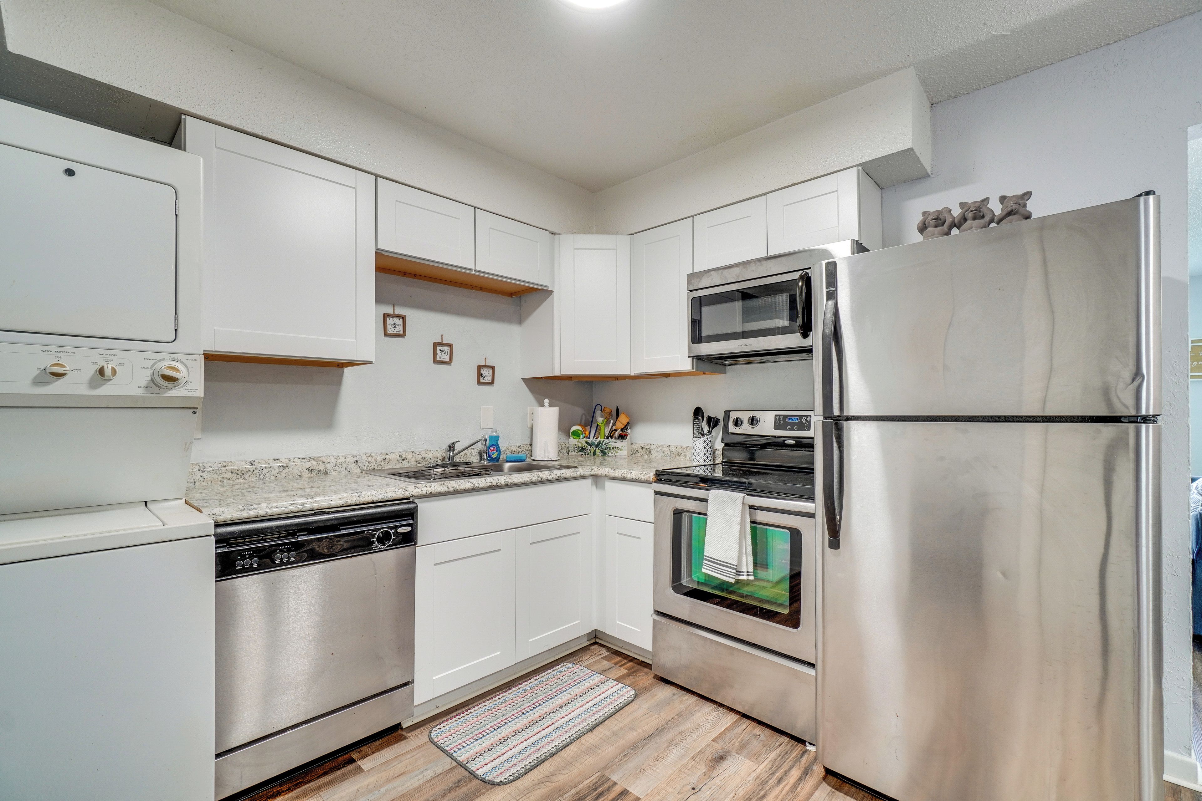 A modern kitchen with stainless steel appliances, white cabinetry, and a wooden floor.