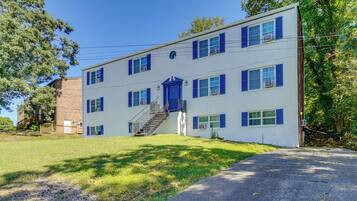 A two-story building with a blue door and windows, a staircase, and a paved driveway.