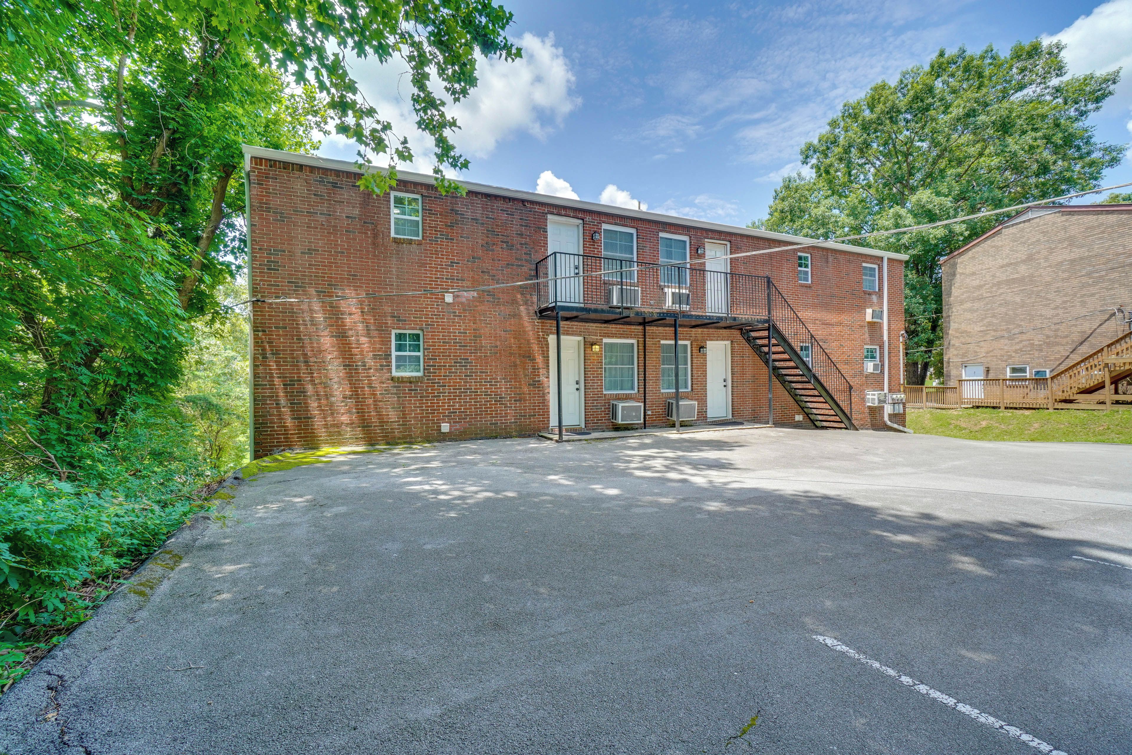 A brick building with a fire escape, a gated entrance, and a paved driveway.
