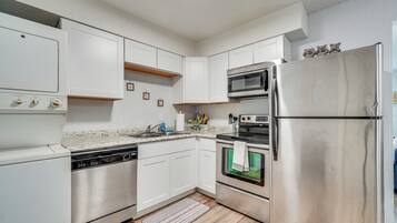 A modern kitchen with stainless steel appliances, white cabinetry, and a wooden floor.
