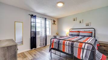 A bedroom with a bed, a desk, a chair, a wardrobe, and a window with curtains.