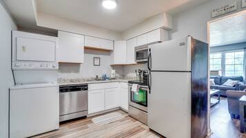A modern kitchen with white cabinetry, stainless steel appliances, and a wooden floor.