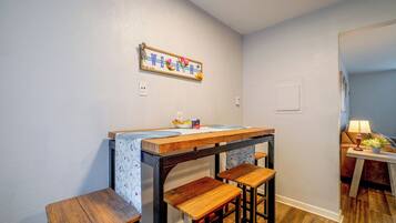 A small kitchen with a wooden table and bar stools, a wall-mounted light switch, and a framed sign above the counter.